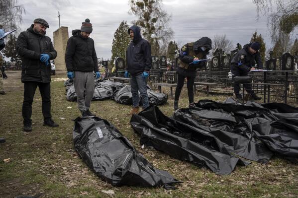 FILE - Vladyslav Minchenko, left, with policemen collect information next to corpses of civilians killed in Bucha, before the corpses are transported to the morgue, on the outskirts of Kyiv, Ukraine, Wednesday, April 6, 2022. (AP Photo/Rodrigo Abd, File)