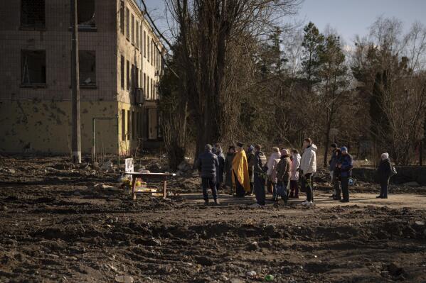 A priest performs a religious service on the place of a building that was demolished after being heavily damaged by an airstrike, one year ago, in memory of those killed in Borodyanka, Ukraine, Thursday, March 2, 2023. Nearly a year after towns and villages near Kyiv were retaken from Russian troops who had seized territory as they raced toward Kyiv at the start of their invasion of Ukraine, authorities are still exhuming the bodies of civilians hastily buried in makeshift graves. (AP Photo/Vadim Ghirda)