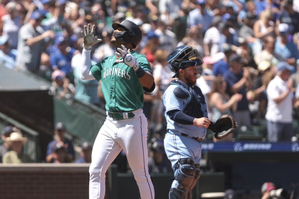Seattle Mariners' Julio Rodriguez, left, celebrates after crossing home plate as Toronto Blue Jays catcher Alejandro Kirk, right, looks on during the third inning of a baseball game, Saturday, July 22, 2023, in Seattle. (AP Photo/Jason Redmond)