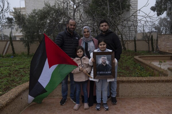 From top left, Hafeth, 40, father, Mona, 36, mother, Amir, 22, brother and from down left, Yaffa, 7, and Rabea, 8, sisters, pose with a framed photo and name, of their slain family member 17-year-old Tawfic Abdel Jabbar, a teenager from Louisiana who was fatally shot last week, at the family's Palestinian home village, Al-Mazra'a ash-Sharqiya, West Bank, Tuesday, Jan. 23, 2024. (AP Photo/Nasser Nasser)