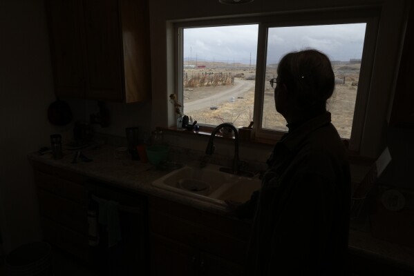 Gayna Salinas looks out her kitchen window at a trailer newly placed on land owned by Anson Resources, who is eyeing an area nearby to extract lithium, Thursday, Jan. 25, 2024, in Green River, Utah. Salinas, whose family farms in the rural community, said she was skeptical about the project's benefits. (AP Photo/Brittany Peterson)