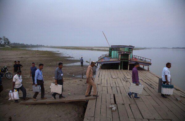 FILE- Election officers carry Electronic Voting Machines (EVM) on board a ferry to cross the Sowansiri river to reach a polling center on the eve OF elections in Majuli, India, March 26, 2021. The 6-week-long general elections will begin on April 19, 2024, and results will be announced on June 4. While voters in the United States and elsewhere use paper ballots, India uses Electronic Voting Machines or EVMs. (AP Photo/Anupam Nath, File)
