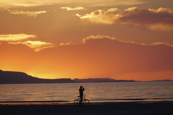A man on a bike photographs the sunset at the Great Salt Lake Thursday June 13, 2024, near Salt Lake City. (AP Photo/Rick Bowmer)