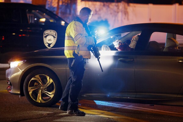 A police officer manning a roadblock talks with an employee of New Hampshire Hospital who was trying to get to work, Friday, Nov. 17, 2023, in Concord, N.H. A shooter killed one person Friday in the lobby of the psychiatric hospital and then was fatally shot by a state trooper, officials said. (AP Photo/Michael Dwyer)