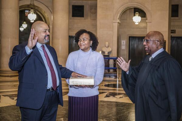 Alvin L. Bragg, Jr., left, place his hand a bible held by his wife Jamila Ponton Bragg, center, as Judge Milton Tingling, right, administers the oath of office and swears him as the first Black Manhattan District Attorney, Friday, Dec. 31, 2021 in New York. (Julie Skarritt/Richard Fife PR via AP)