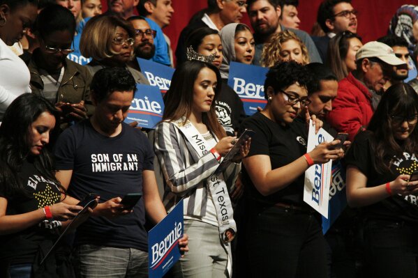 Supporters of Democratic presidential candidate Sen. Bernie Sanders I-Vt. text a phone number to find their closet polling place at a campaign event in El Paso, Texas, Saturday, Feb. 22, 2020. (AP Photo/Cedar Attanasio)