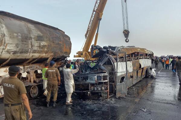 Police officers and workers remove the wreckage of a bus that collided with an oil tanker along a highway in Uch Sharif near Multan, Pakistan, Tuesday, Aug. 16, 2022. A truck rammed into a minibus on a highway in eastern Pakistan overnight, causing a fire that killed and injured numerous passengers, a rescue official said Monday. (AP Photo)
