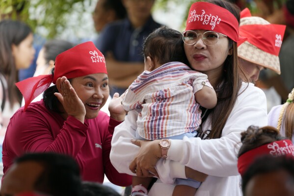A participant plays with a child as they attend a celebration to mark the International Women's Day at Freedom Park in Phnom Penh Cambodia, Friday, March 8, 2024. The headband reads "Dignified life." (AP Photo/Heng Sinith)