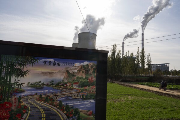 A resident rides past the Guohua Power Station in Dingzhou, Baoding in the northern China's Hebei province, Friday, Nov. 10, 2023. China and the U.S. have pledged to accelerate their efforts to address climate change ahead of a major U.N. meeting on the issue, making a commitment to take steps to reduce emissions of methane and other greenhouse gases besides carbon dioxide. (AP Photo/Ng Han Guan)