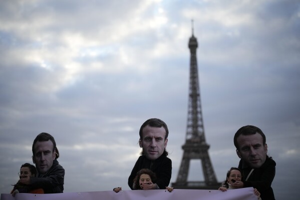 Gagged activists hold a placard as persons wearing a mask of French President Emmanuel Macron stand behind putting his hand on their mouth during a protest Friday, Nov. 24, 2023 in Paris. Activists say that France is vetoing a European decision on rape definition based on lack of consent. The large majority of EU member countries already treat violence against women and girls as a crime but the Commission said last year there are gaps in national legislation. (AP Photo/Christophe Ena)