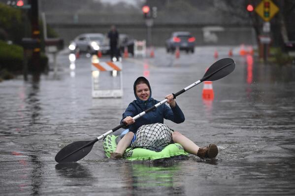 Nurse Katie Leonard uses a kayak to bring supplies to Patsy Costello, 88, as she sits trapped in her vehicle for over an hour on Astrid Drive in Pleasant Hill, Calif., on Saturday, Dec. 31, 2022. Costello drove her car on the flooded street thinking she could make it when it stalled in the two feet of water. After two hours the water had receded about a foot making it easier to rescue her. Police were called but stood by and watched after calling in a tow truck to help pull the car out of the water. Nurse Katie Leonard, of Pleasant Hill, lives down the block used her kayak to bring Costello hot tea, blankets, food and a phone to call a friend. (Jose Carlos Fajardo/Bay Area News Group via AP)