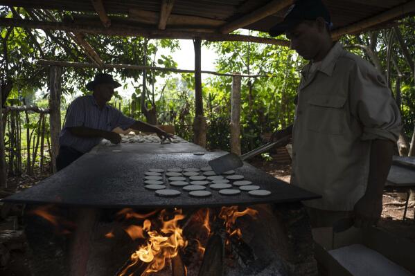 Casabe producer Julio Cesar Nunez, left, and his nephew Agustin cook small cakes of casabe on a griddle over a wood fire, in Quivican, Cuba, Monday, May 28, 2023. When Nunez, 80, was a child, he helped his grandmother make casabe from scratch, using artisanal tools — and an ancient cooking method — to turn grated yuca root into a thin, white, crispy flatbread. (AP Photo/Ramon Espinosa)