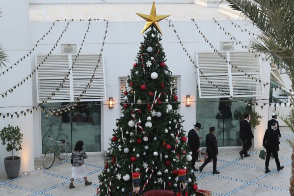 A rabbi and other guests pass a Christmas tree to take part in an Israeli wedding ceremoney in Dubai, United Arab Emirates, Thursday, Dec. 17, 2020.  For the past month, Israelis long accustomed to traveling incognito, if at all, to Arab countries, have made themselves at home in the UAE’s commercial hub. (AP Photo/Kamran Jebreili)