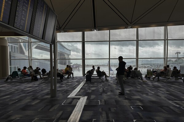 Travelers wait at the departures hall at Hong Kong International Airport in Hong Kong, Sunday, Oct. 8, 2023. Scores of flights in Hong Kong were canceled Sunday as Tropical Storm Koinu neared the southern Chinese city after leaving at least one dead and over 300 injured in Taiwan. (AP Photo/Emily Wang)