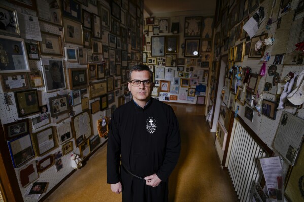 The Rev. Francesco Di Feliciantonio poses for portraits in a room of the St. Gabriele dell'Addolorata sanctuary in Isola del Gran Sasso near Teramo in central Italy, filled with votive offerings, from baby bibs to sports jerseys, left by two million annual visitors to St. Gabriele, Sunday, June 4, 2023. (AP Photo/Domenico Stinellis)