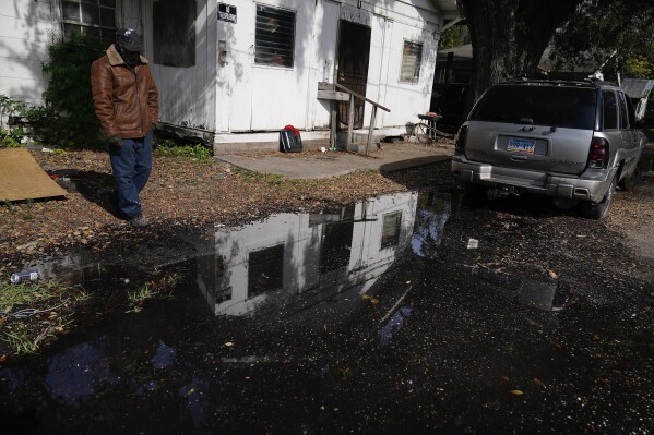 A man stands near his home looking at a street he says has been flooded for months, on Thursday, Dec. 7, 2023, in Prichard, Ala. Up to 60% of the city’s water leaks from a decrepit distribution system. Communities nationwide are losing trillions of gallons. (AP Photo/Brynn Anderson)