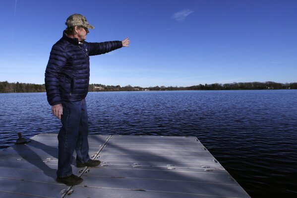 In this Dec. 27, 2018, photograph, Murray Beach, an investment banker who lives on the shore of Willett Pond, points out the pond’s spillway across the water in Walpole, Mass. The spillway at the 107-year-old Willett Pond Dam is capable of handling just 13% of the water flow from a serious flood before the dam is overtopped, according to a recent state inspection report. “We are not talking of just flooding someone’s house. We are talking about covering their house,” said Beach, who belongs to a citizens group that has lobbied for years for the spillway to be repaired.(AP Photo/Charles Krupa)