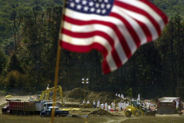 FILE — An American flag flies from a makeshift altar overlooking the ongoing investigation of the United Flight 93 crash site, in Shanksville, Pa., Sept. 16, 2001. Americans are looking back on the horror and legacy of 9/11, gathering Monday, Sept. 11, 2023, at memorials, firehouses, city halls and elsewhere to observe the 22nd anniversary of the deadliest terror attack on U.S. soil. (AP Photo/Gene J. Puskar, File)