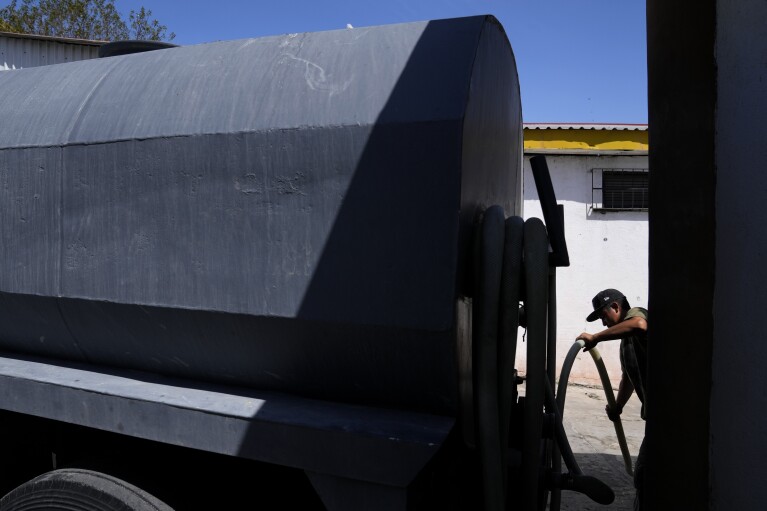 Jose Manuel Perez Reyes uncoils a hose as he delivers water to auto mechanic shop from his water truck Tuesday, May 9, 2023, in Tijuana, Mexico. Among the last cities downstream to receive water from the shrinking Colorado River, Tijuana is staring down a water crisis. (AP Photo/Gregory Bull)