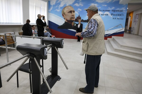 A man leaves a polling station with a billboard in background with an image of Russian President Vladimir Putin and reading 