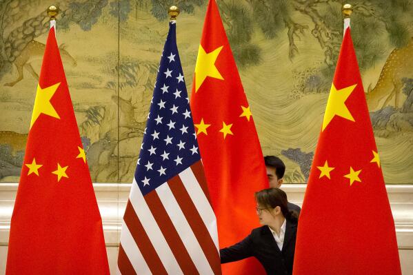 FILE - In this Feb. 14, 2019, file photo, Chinese staffers adjust the U.S. and Chinese flags before the opening session of trade negotiations between U.S. and Chinese trade representatives at the Diaoyutai State Guesthouse in Beijing. In a relationship as fraught as America's and China's, just an agreement that talks were productive was a sign of progress. Nine months into Joe Biden's presidency, the two sides finally appear to be trying to ease tensions that date from the Trump administration — though U.S. complaints about Chinese policies on trade, Taiwan and other issues are little diminished. (AP Photo/Mark Schiefelbein, File)
