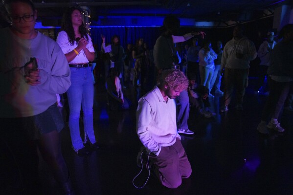 Haynza Posala, 23, center, kneels in prayer during an impromptu worship session at the end of The Cove's third event on Saturday, Feb. 17, 2024, in Nashville, Tenn. (AP Photo/Jessie Wardarski)