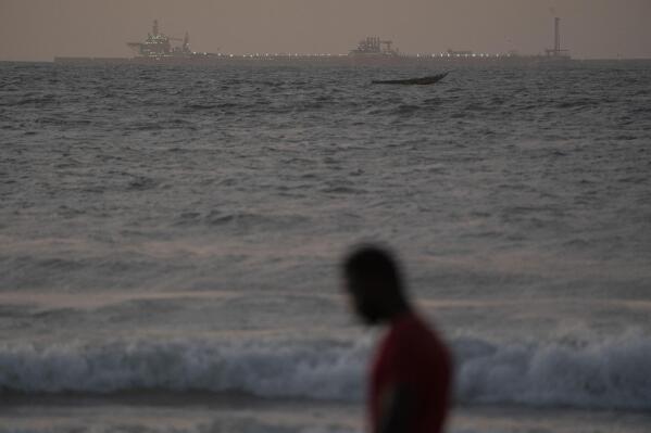 A man walks on the beach past an offshore gas terminal in Saint Louis, Senegal, Thursday, Jan. 19, 2023. The rig was the final straw for Saint-Louis, pushing it to the brink of economic disaster, according to locals, officials and advocates. (AP Photo/Leo Correa)