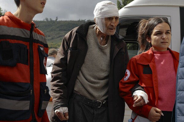 Wounded ethnic Armenian man named Sasha, 84 years-old, from Stepanakert, Nagorno-Karabakh is helped by volunteers walk as he arrives in Armenia's Goris in Syunik region, Armenia, on Wednesday, Sept. 27, 2023. Some 42,500 people, or about 35% of Nagorno-Karabakh's ethnic Armenian population, has left for neighboring Armenia as of Wednesday morning, according to Armenian authorities. Hours-long traffic jams were reported on Tuesday on the road linking Nagorno-Karabakh to Armenia. (AP Photo/Vasily Krestyaninov)