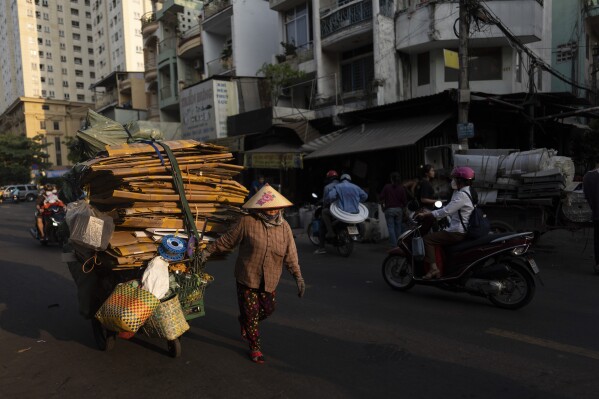 A woman hauls a cart full of cardboard for recycling as the sun sets in Nhat Tao market, the largest informal recycling market in Ho Chi Minh City, Vietnam, Wednesday, Jan. 31, 2024. (AP Photo/Jae C. Hong)