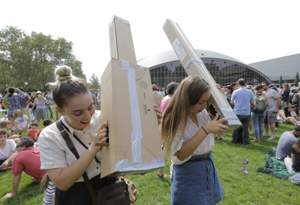 FILE - Reveka Pasternak, of Boston, left, and her sister Tristen, of Philadelphia, right, use pinhole projectors to view a partial solar eclipse, Monday, Aug. 21, 2017, on the campus of Massachusetts Institute of Technology, in Cambridge, Mass. The sisters made the pinhole projectors from cardboard that allow people to safely view the eclipse. (AP Photo/Steven Senne, File)