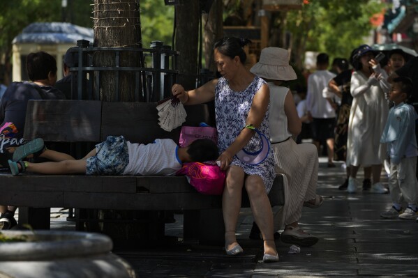 A woman uses a fan to cool a child as they sit on a bench at Qianmen pedestrian shopping street on a hot day in Beijing, Thursday, June 29, 2023. (AP Photo/Andy Wong)