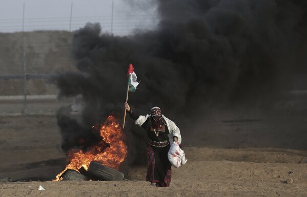 
              FILE - In this Oct. 5, 2018 file photo, a Palestinian woman carries a Palestinian flag during a protest at the Gaza Strip's border with Israel. Hamas controls Gaza more tightly than ever, despite unprecedented domestic unrest and its failure to significantly weaken Israel's chokehold of the territory after a year of weekly anti-blockade rallies along their shared frontier. (AP Photo/Khalil Hamra, File)
            