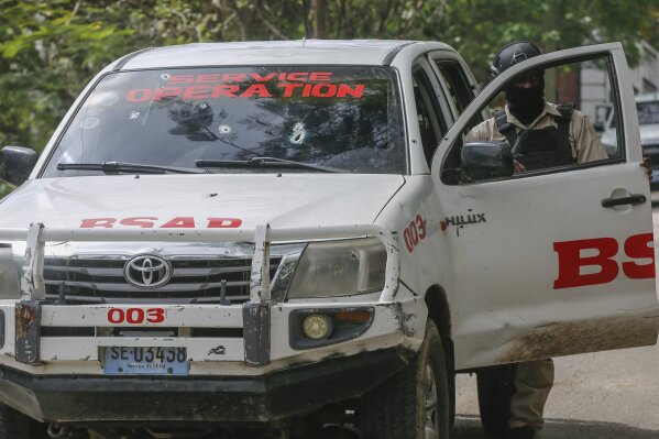 A police officer inspects a Protected Areas Security Brigade (BSAP) vehicle with gunshot holes in its windshield, on the third consecutive day of protests demanding the resignation of Prime Minister Ariel Henry, in Port-au-Prince, Haiti, Wednesday, Feb. 7, 2024. (AP Photo/Odelyn Joseph )