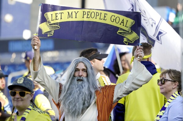 FILE - Stephen Mason, dressed as "Soccer Moses," holds up a sign which reads, "Let my people goal" before an MLS soccer match between Nashville SC and New York Red Bulls Sunday, Nov. 7, 2021, in Nashville, Tenn. His face flies on a flag outside the Nashville new stadium and he’s often found in the team’s supporter section, where its most devoted fans gather. (AP Photo/Mark Humphrey, File)