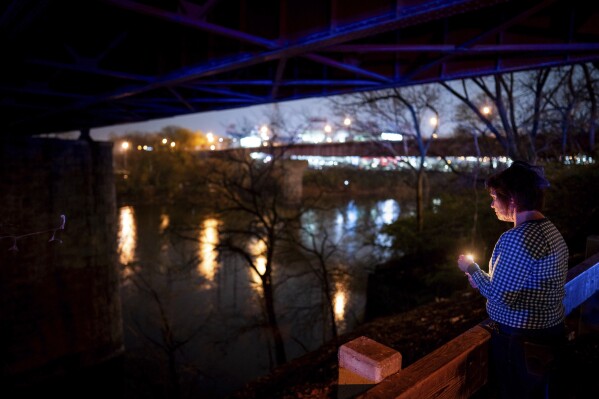 Kelly Granger, of Nashville, holds a candle while looking out at the Cumberland River during a vigil for Riley Strain on Gay Street in Nashville, Tenn., Friday, March 22, 2024. The body of the missing University of Missouri student was discovered early Friday in the Cumberland River. (Andrew Nelles/The Tennessean via AP)