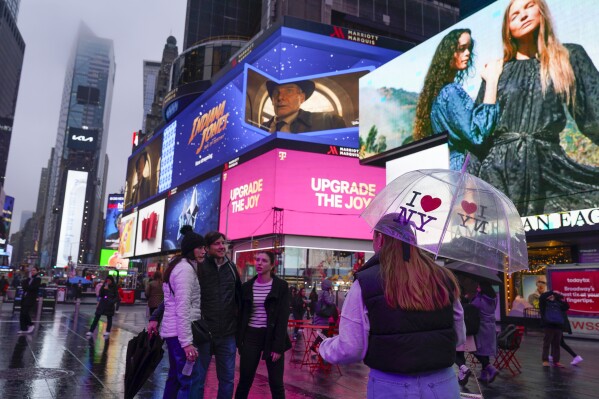 Pedestrians stop to take a picture in a wet and foggy Times Square in New York, Monday, Dec. 18, 2023. A storm moving up the East Coast brought heavy rain and high winds to the Northeast on Monday, threatening flooding, knocking out power to hundreds of thousands, and forcing flight cancelations and school closings. (AP Photo/Seth Wenig)