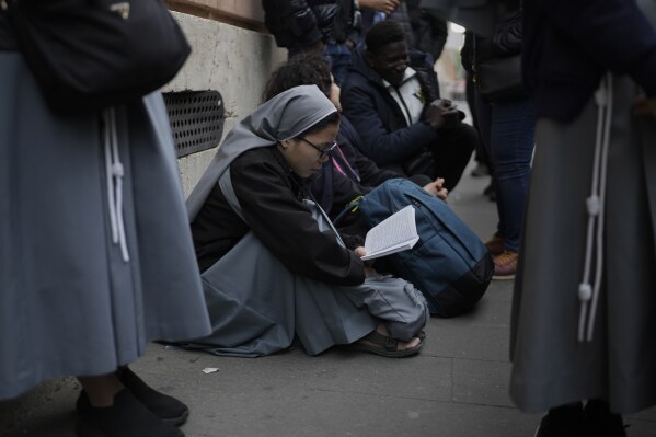 A nun reads a book as she waits in line with others to view Pope Francis lying in state inside St. Peter's Basilica, at the Vatican, Thursday, April 24, 2025. (AP Photo/Markus Schreiber)