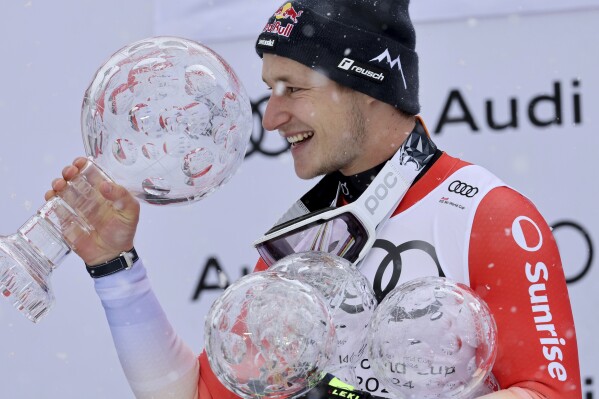 Switzerland's Marco Odermatt holds the alpine ski World Cup overall title trophy, left, and the trophies for downhill, super-G and giant slalom disciplines as he celebrates on the podium, in Saalbach, Austria, Sunday, March 24, 2024. (AP Photo/Marco Trovati)