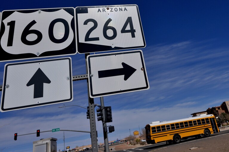 A school bus crosses over U.S. 160 from the Navajo Nation, left, onto the Hopi reservation, right, Monday, March 4, 2024, in Tuba City, Ariz. U.S. Highway 160 is the de facto border between the Navajo and Hopi Indian reservations and two time zones. Mind-bending time calculations is what people in the largest Native American reservation in the U.S. have to endure every March through November. The Navajo Nation, which stretches into Utah and New Mexico, will reset clocks for one hour later despite the rest of Arizona remaining on standard time. (AP Photo/Matt York)