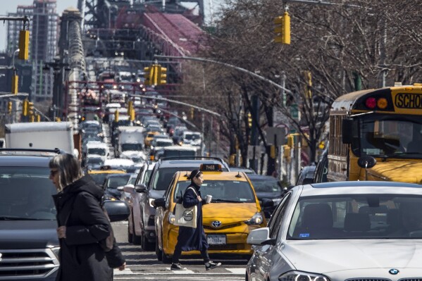 FILE - Pedestrians cross Delancey Street as congested traffic from Brooklyn enters Manhattan over the Williamsburg Bridge, March 28, 2019, in New York. New York Gov. Kathy Hochul is trying to raise taxes on businesses in the city to close a big budget gap that emerged after she halted a plan to charge drivers a toll to enter the center of Manhattan. (AP Photo/Mary Altaffer, File)