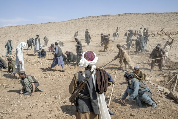 A Taliban fighter, foreground, watches over laborers building a road in a remote region of Afghanistan, on Saturday, Feb. 25, 2023. In a nearby village, a baby was orphaned during a U.S. raid in 2019. A Marine who adopted her claims her parents were foreign fighters. But villagers say they were innocent farmers caught in the fray. (AP Photo/Ebrahim Noroozi)