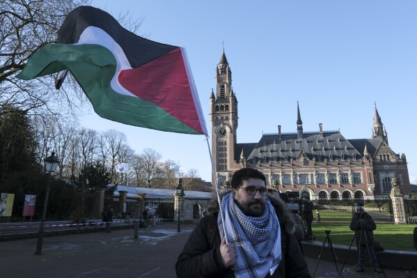 A protester waving the Palestinian flag stands outside the Peace Palace, which houses the International Court of Justice, or World Court, in The Hague, Netherlands, Friday, Jan. 26, 2024. Israel is set to hear whether the United Nations' top court will order it to end its military offensive in Gaza during a case filed by South Africa accusing Israel of genocide. (AP Photo/Patrick Post)
