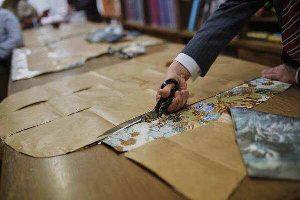 A tailor uses a pattern to cut fabric at the Gammarelli ecclesiastic clothes tailor shop in Rome, Wednesday, April 30, 2025. (AP Photo/Francisco Seco)