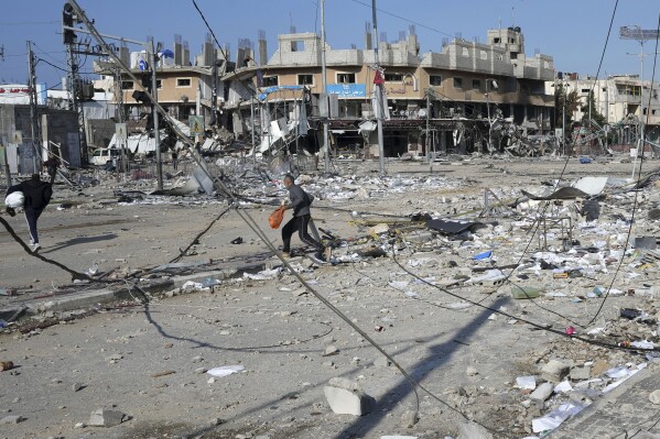 Palestinians walk through destruction by the Israeli bombardment in the Nusseirat refugee camp in Gaza Strip, Tuesday, Jan. 16, 2024. (AP Photo/Adel Hana)
