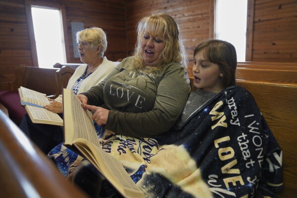 Sheri Taylor, left, sits with her daughter, Laura Wood, and granddaughter, Riley McKibbin, 11, while singing from "The Sacred Harp" in the tenor section at Holly Springs Primitive Baptist Church in Bremen, Ga., on Saturday, March 22, 2025. (AP Photo/Jessie Wardarski)
