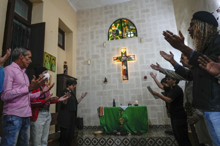 Same-sex couples stand in prayer with outstretched hands inside the Metropolitan Community Church, an LGBTQ+ inclusive house of worship, in Matanzas, Cuba, Friday, Feb. 2, 2024. Cuba repressed gay people after its 1959 revolution led by Fidel Castro and sent many to labor camps. (AP Photo/Ramon Espinosa)