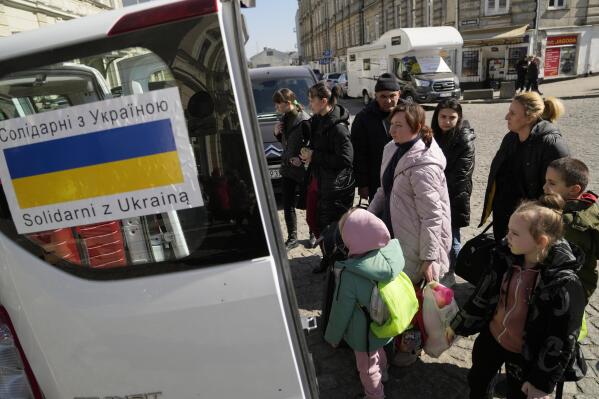 Ukrainian refugees with children board transport at a square next to a railway station in Przemysl, Poland, on Tuesday, March 22, 2022. (AP Photo/Sergei Grits)