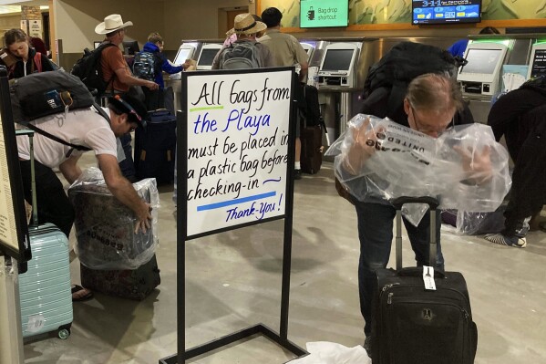 Burning Man attendees place plastic bags over the baggage at the Reno-Tahoe International Airport, Tuesday, Sept. 5, 2023, in Reno, Nev., after leaving the annual festival in the Black Rock Desert, about 100 miles northeast of Reno, that was flooded by heavy rain over the weekend. (AP Photo/Scott Sonner)