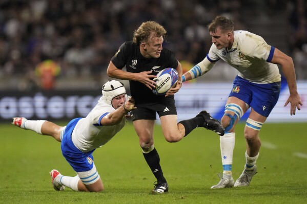 New Zealand's Damian McKenzie, center is tackled by Italy's Manuel Zuliani, left, during the Rugby World Cup Pool A match between New Zealand and Italy at the OL Stadium in Lyon, France, Friday, Sept. 29, 2023. (AP Photo/Pavel Golovkin)