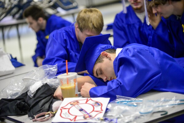 FILE - Chad Burnett, a graduating senior from Hinsdale, N.H. Middle High School, takes a small nap before the commencement ceremony on Saturday, June 17, 2023. The Gallup survey, released Monday, April 15, 2024, says that a majority of Americans say they would feel better if they could have more sleep. But in the U.S., where the ethos of grinding and pulling yourself up by your own bootstraps is ubiquitous, getting enough sleep can seem like a dream.(Kristopher Radder/The Brattleboro Reformer via AP, File)